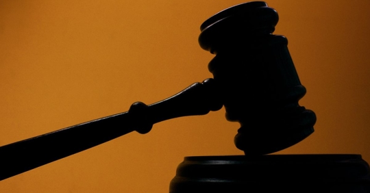 Judge's gavel on a block in front of an orange background.